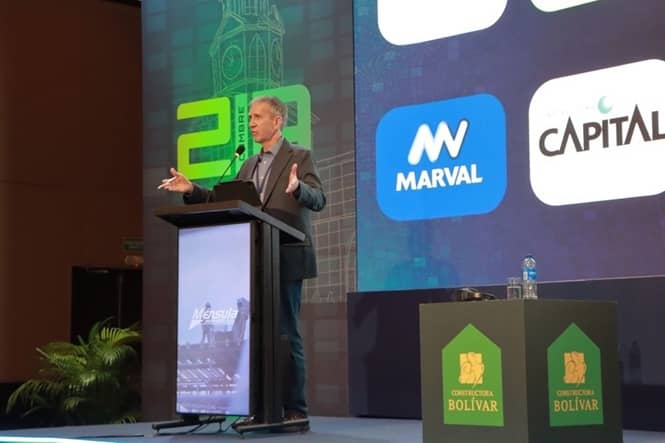 Jeff Crume mid-gesture at the lectern of the CAMACOL artificial intelligence summit, the event's screen behind him